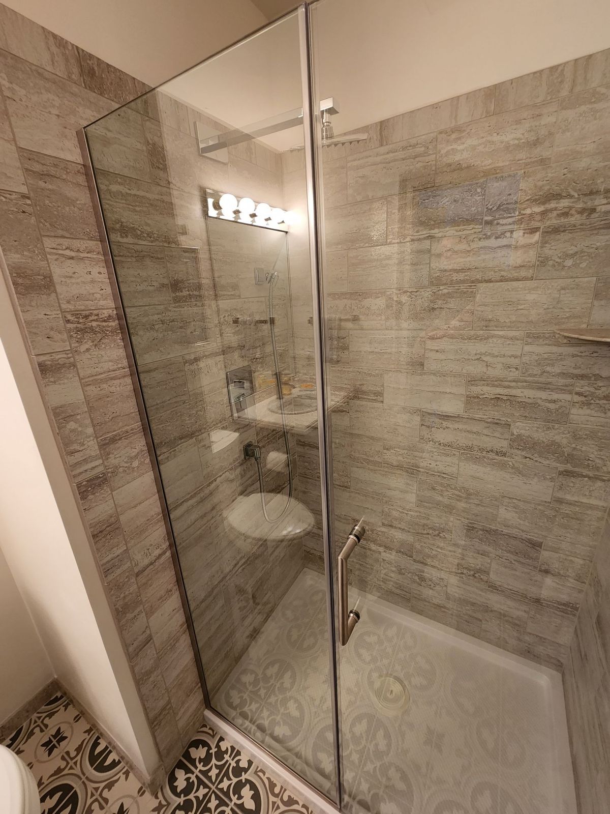 Frameless glass shower stall with travertine tile, angled view