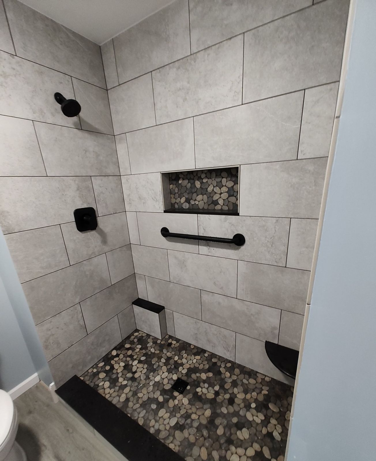 Finished shower with grey stone-look tile, black grab bar, and pebble niche