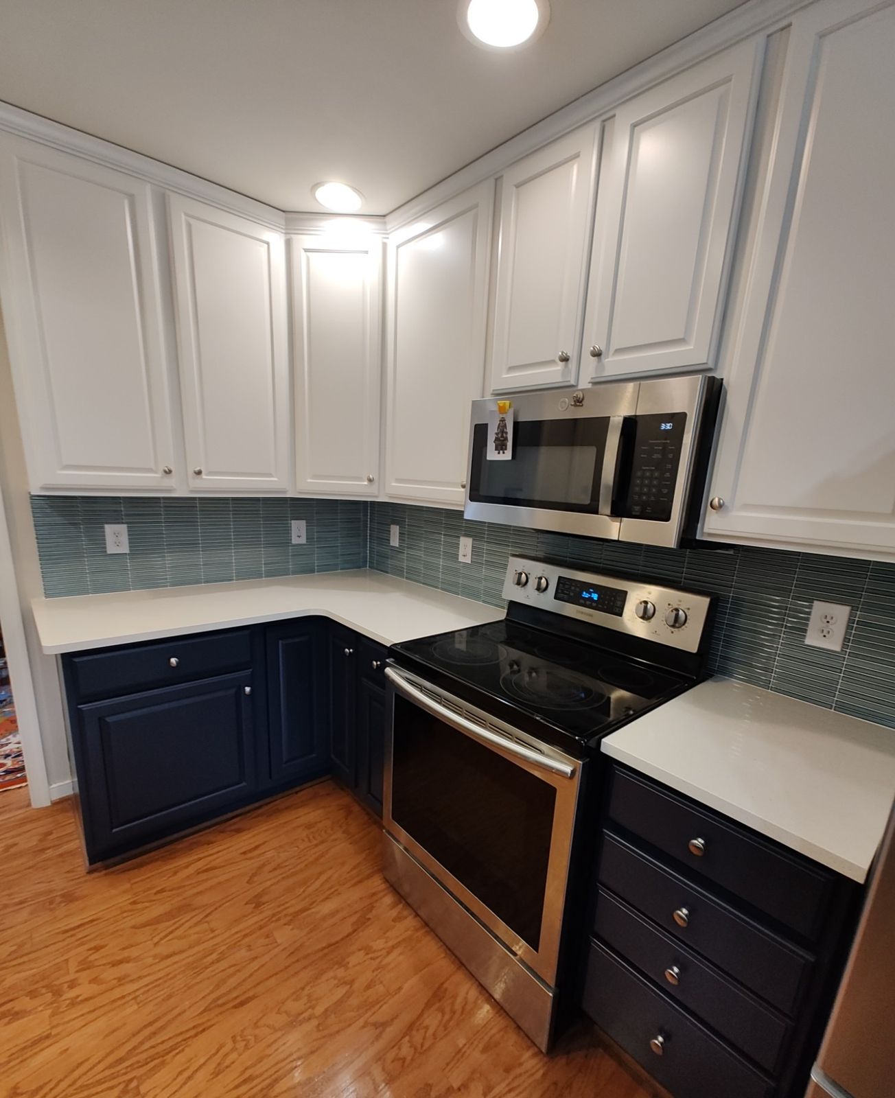 Kitchen with white upper cabinets, navy lower cabinets, and teal glass tile backsplash
