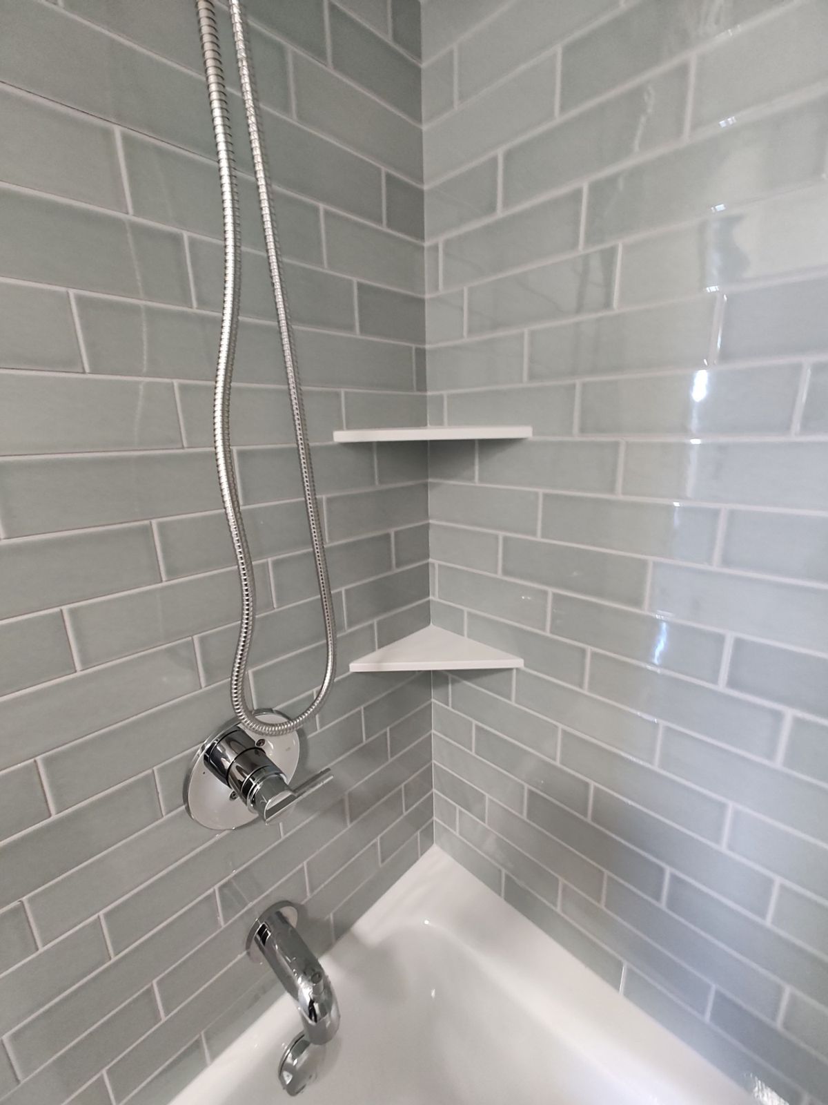 Grey subway tile tub surround with corner shelves and handheld shower head