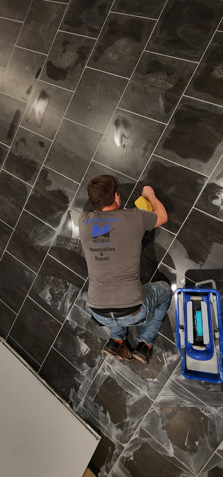 Noble Services crew member grouting a dark tile floor