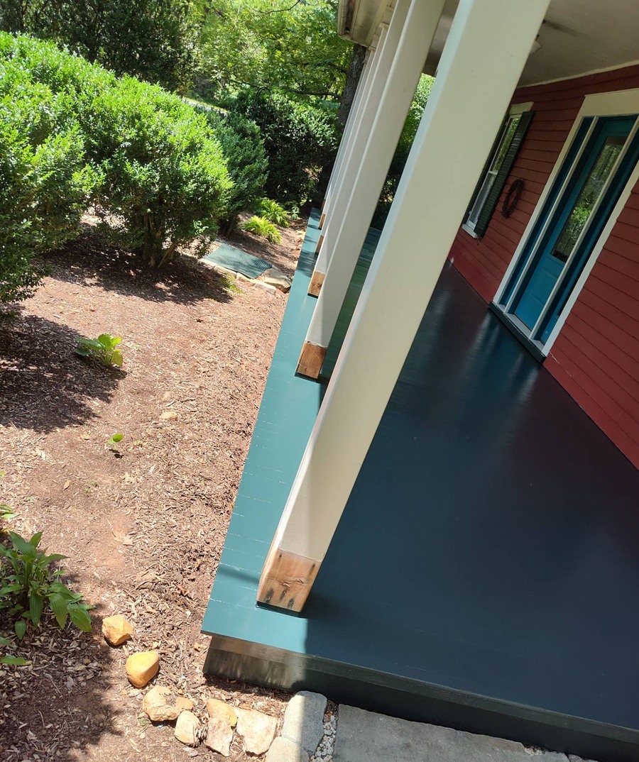 Close-up of a freshly painted teal and navy porch floor against red siding